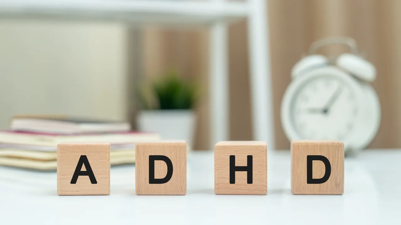 Wooden blocks spell ADHD on a desk with a clock in the background