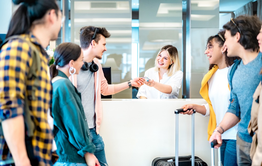 Young travelers checking into a hotel at the front desk while receiving a room key from a receptionist