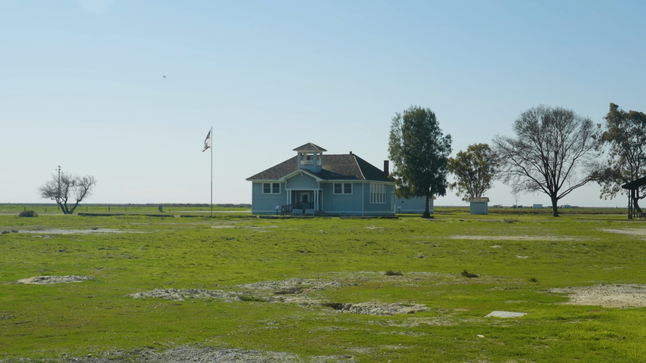 A blue historic schoolhouse stands in a green field at Colonel Allensworth State Historic Park