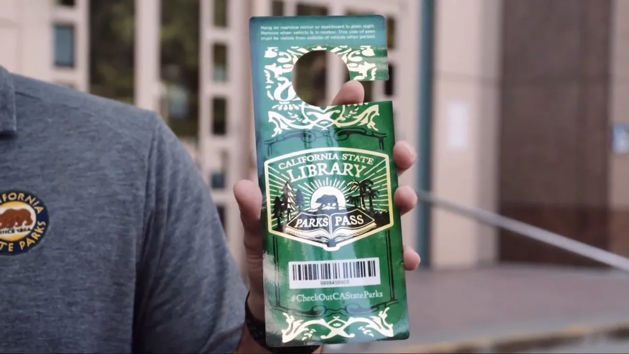 A person holds a California State Library Parks Pass card near a public entrance