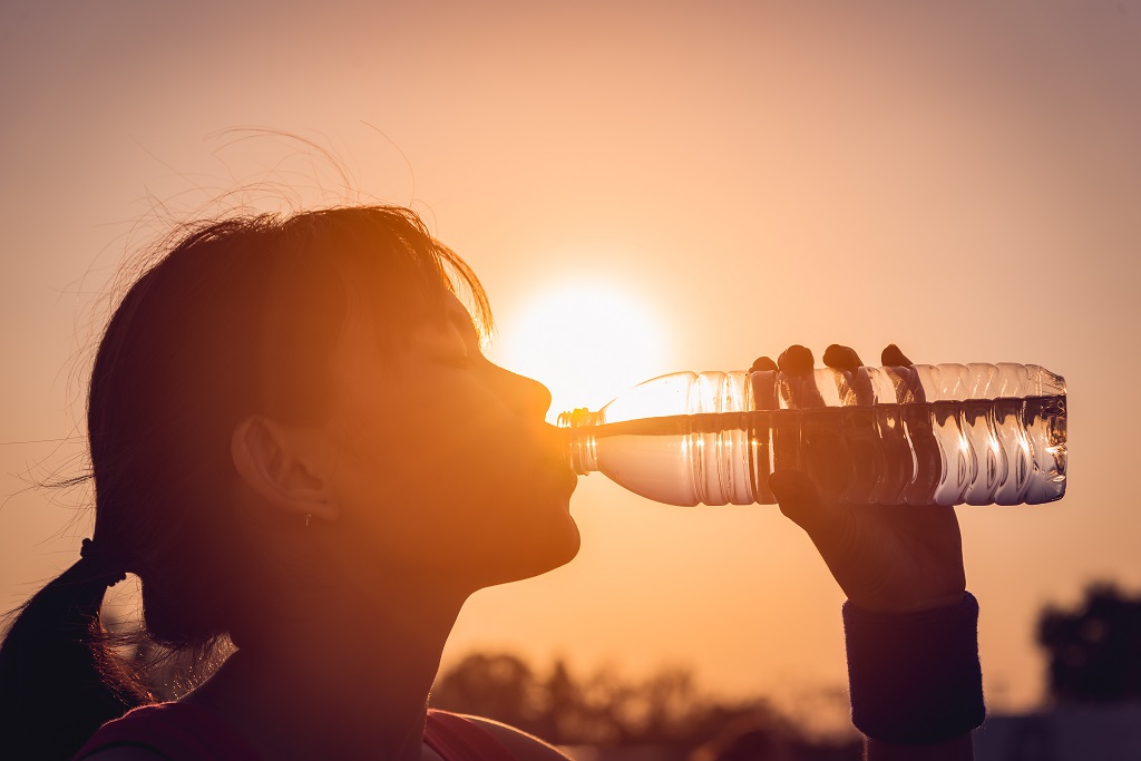 Person drinking water outdoors during a hot summer day with the sun low on the horizon