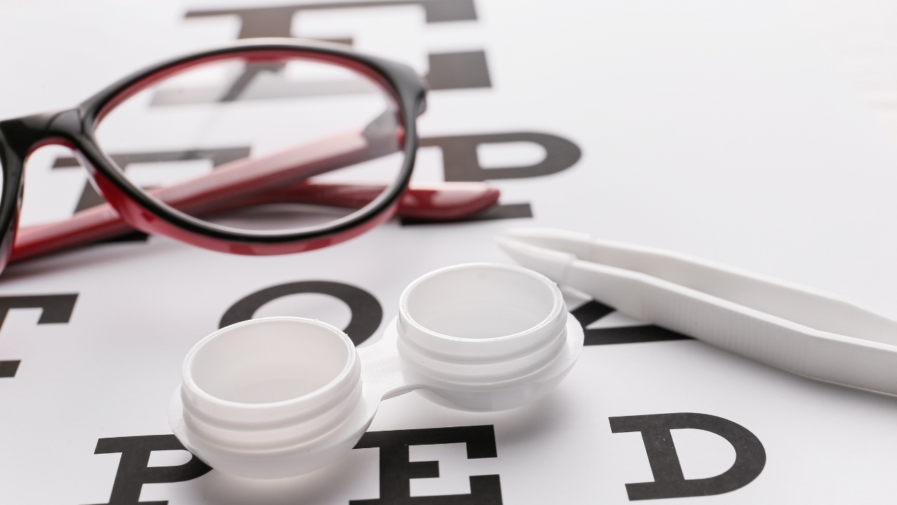 Glasses, a contact lens case, and tweezers rest on an eye chart