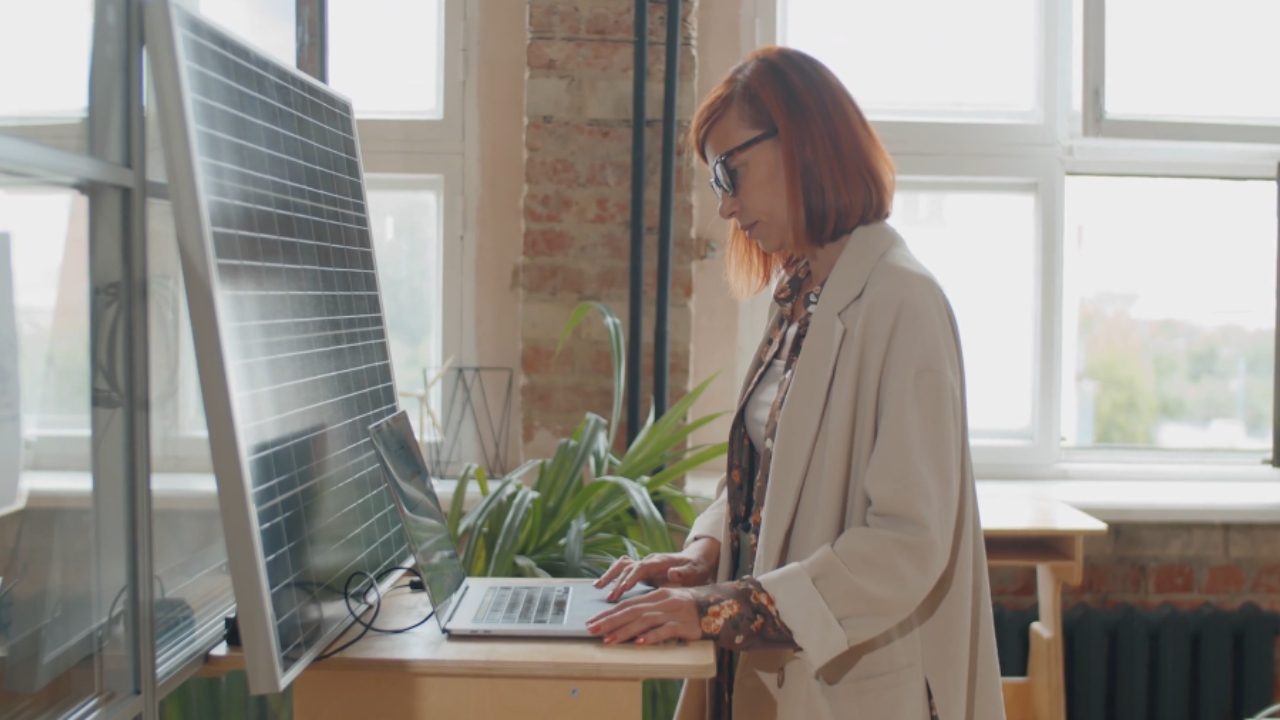 Woman uses a laptop at a height-adjustable desk in a bright office