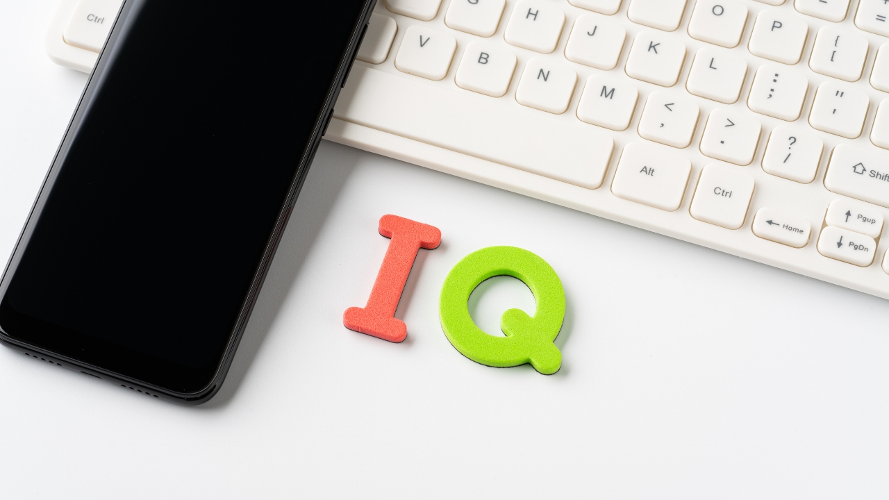 IQ letters beside a smartphone and keyboard on a white desk