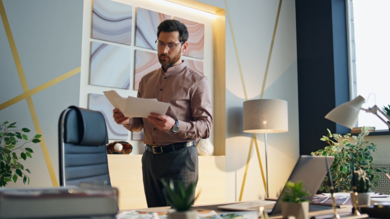 Man reviews papers beside a laptop in a modern office
