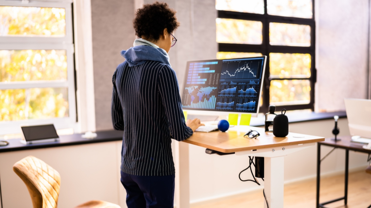 Person works at a height-adjustable desk in a bright office