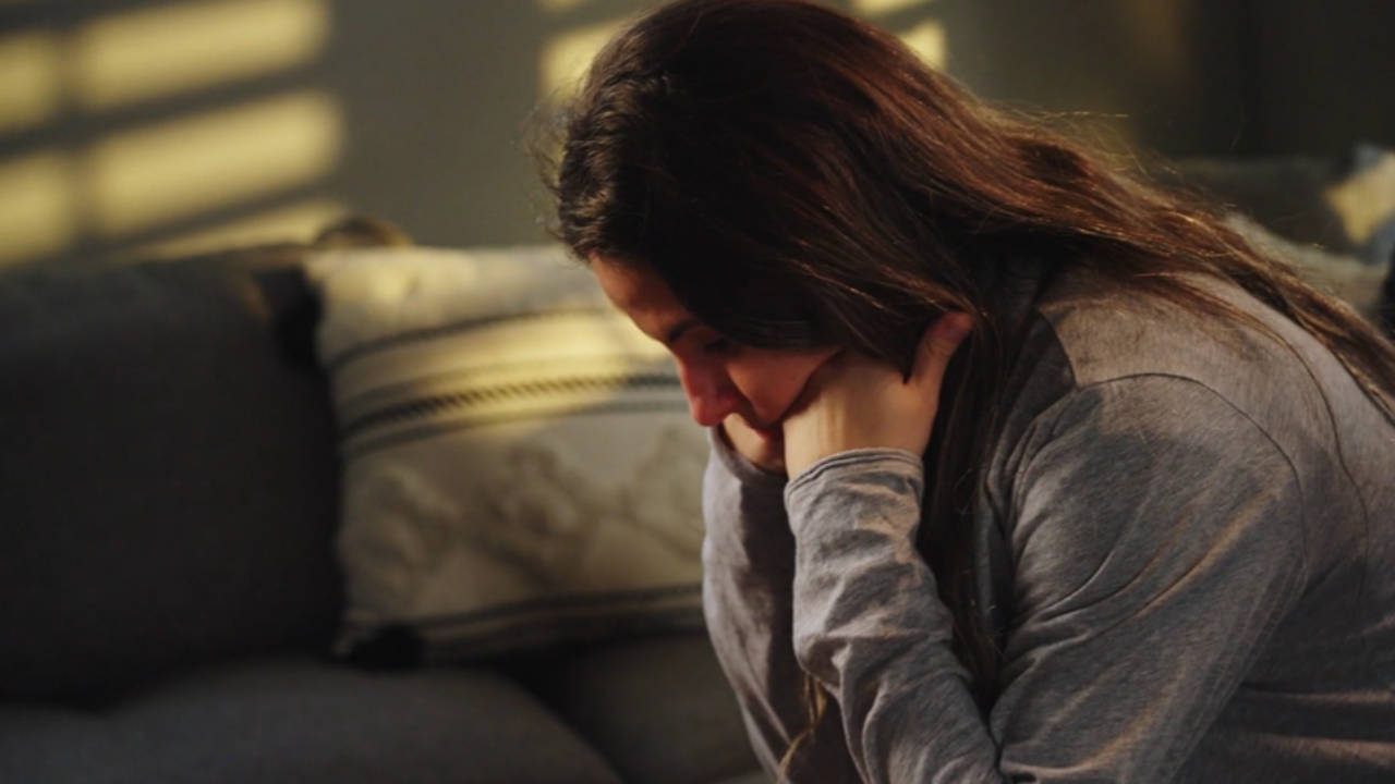 A woman sits on a couch with her head in her hands