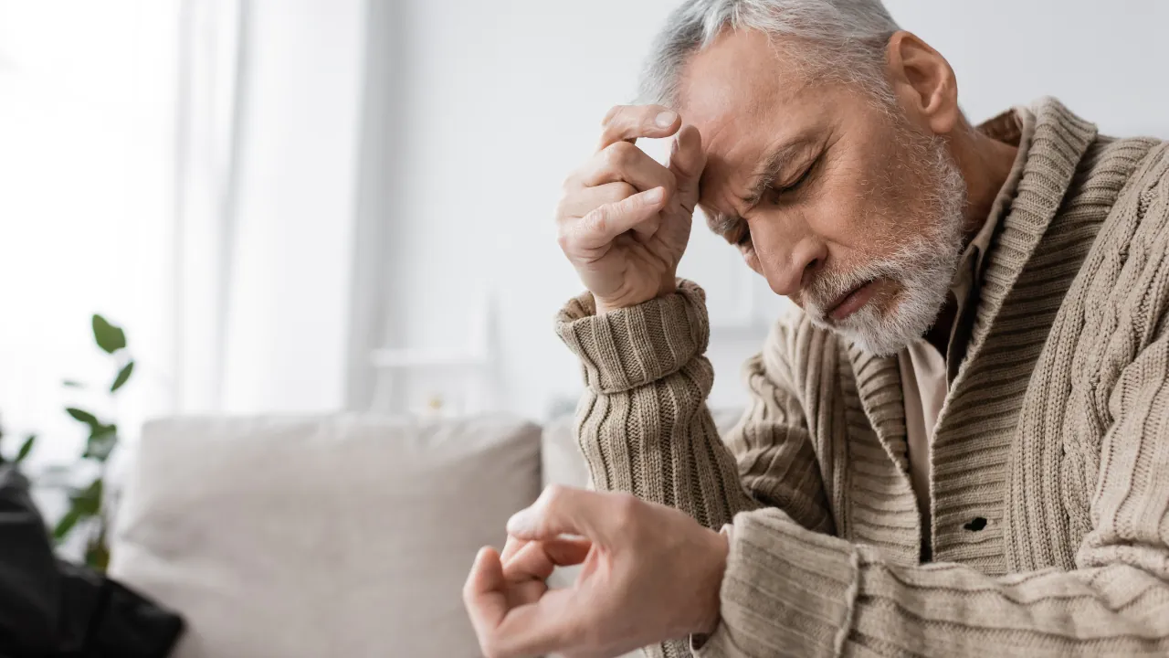 Older man with Parkinson's disease sits at home with his hand on his forehead