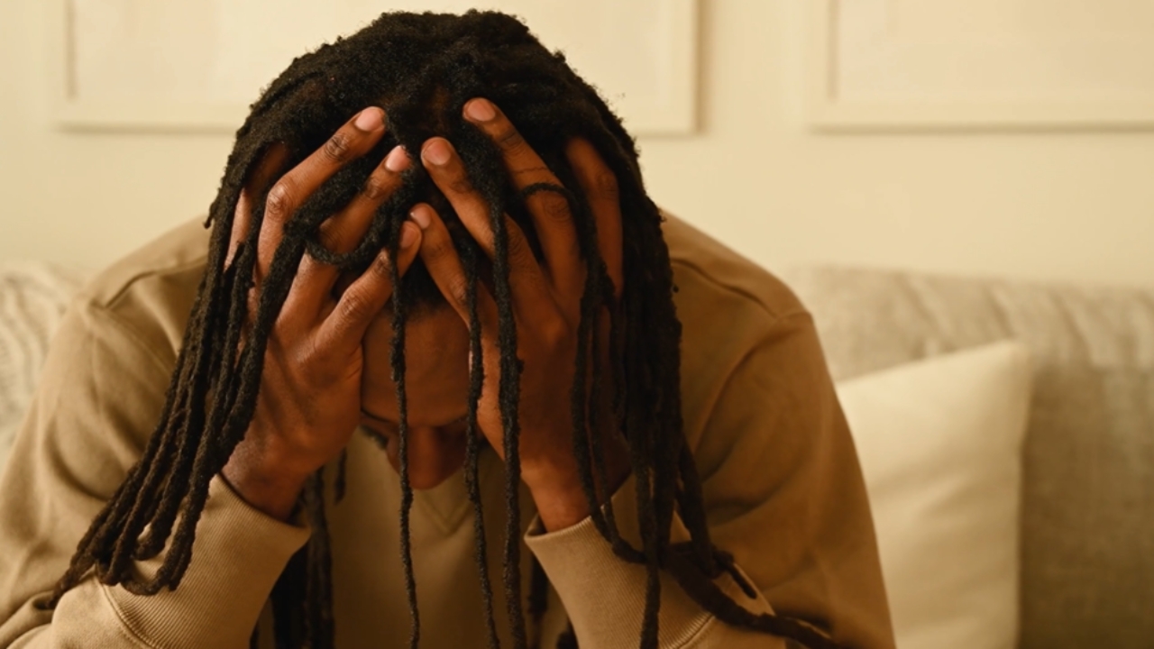 A man covers his face with both hands on a couch