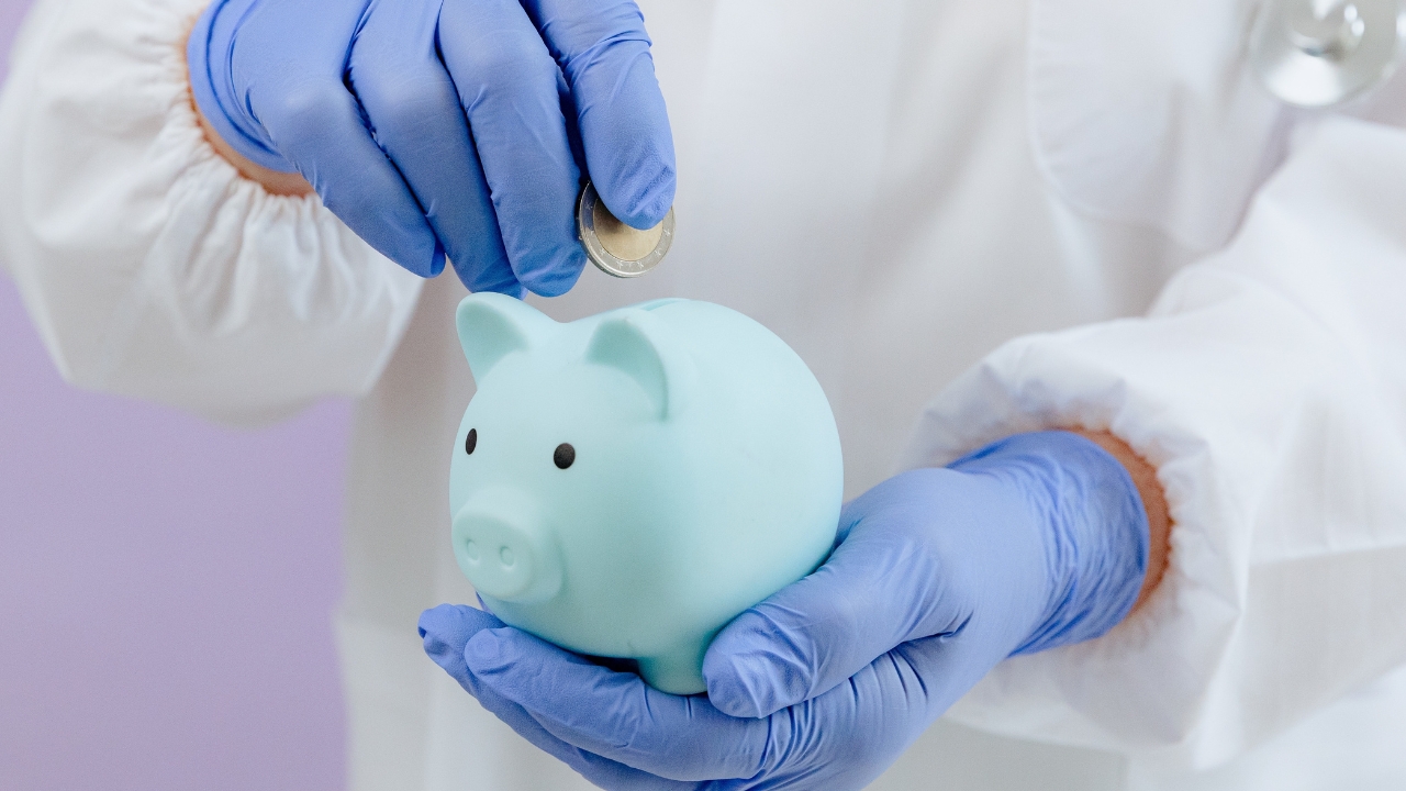 A doctor puts a coin into a piggy bank for health costs