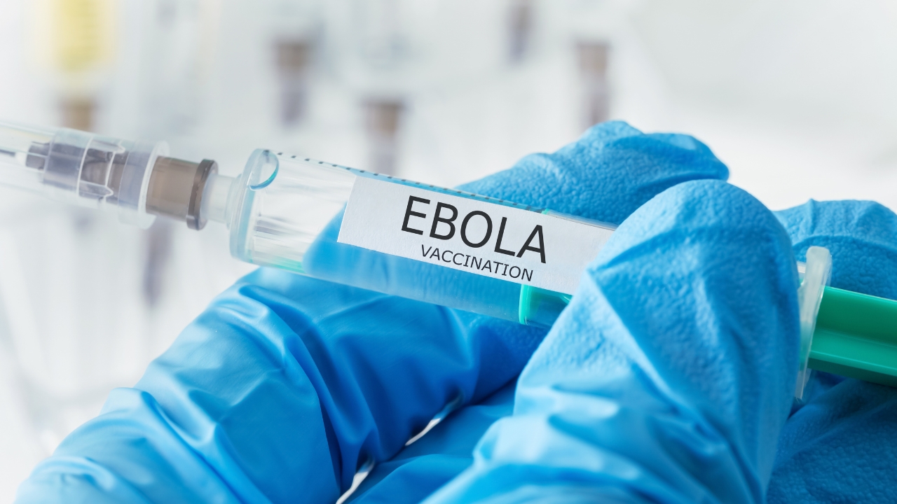 Gloved hands hold a syringe labeled Ebola vaccination