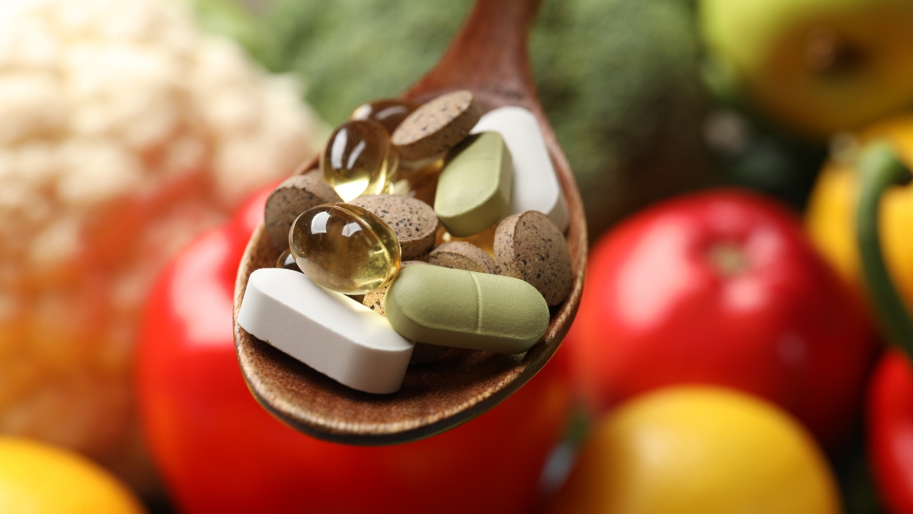 Dietary supplements on a spoon with fresh produce in the background