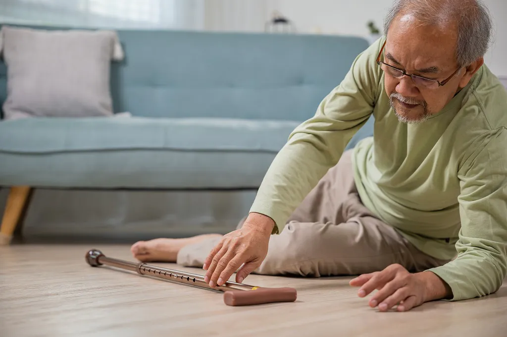 Older man sitting on the floor reaching for a walking cane, illustrating fall risk and the limits of routine vitamin D and calcium supplementation
