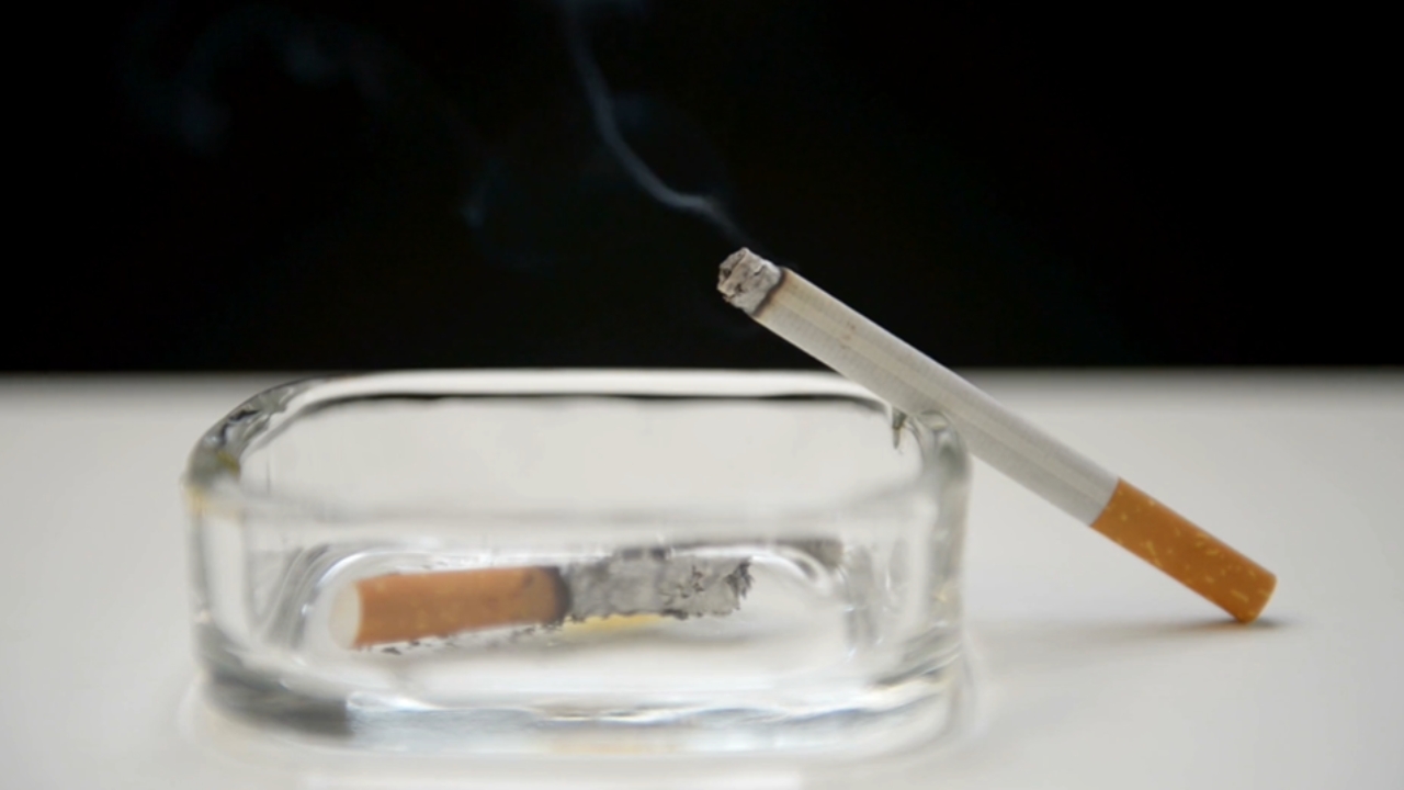A lit cigarette rests on a glass ashtray