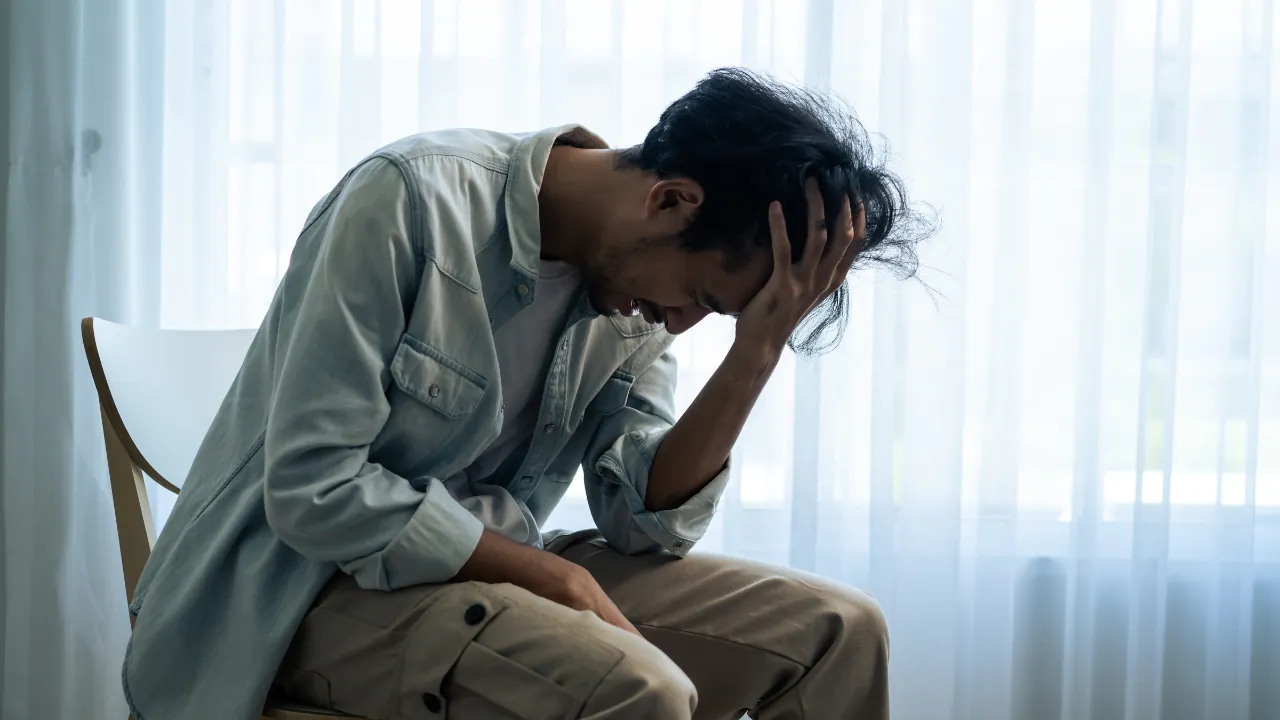 Man sitting with his head in his hand near a bright window
