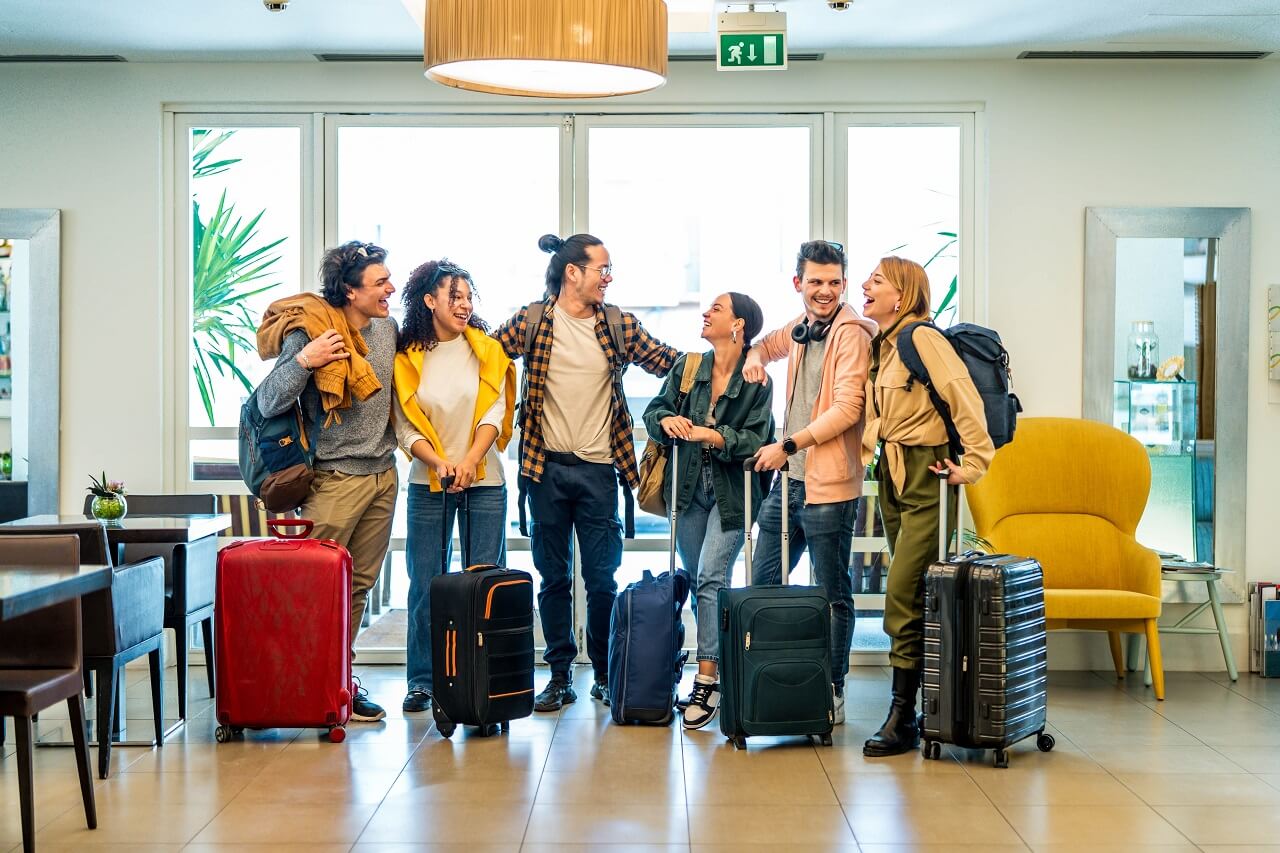 Group of young adult travelers standing in a hotel lobby with luggage before check-in