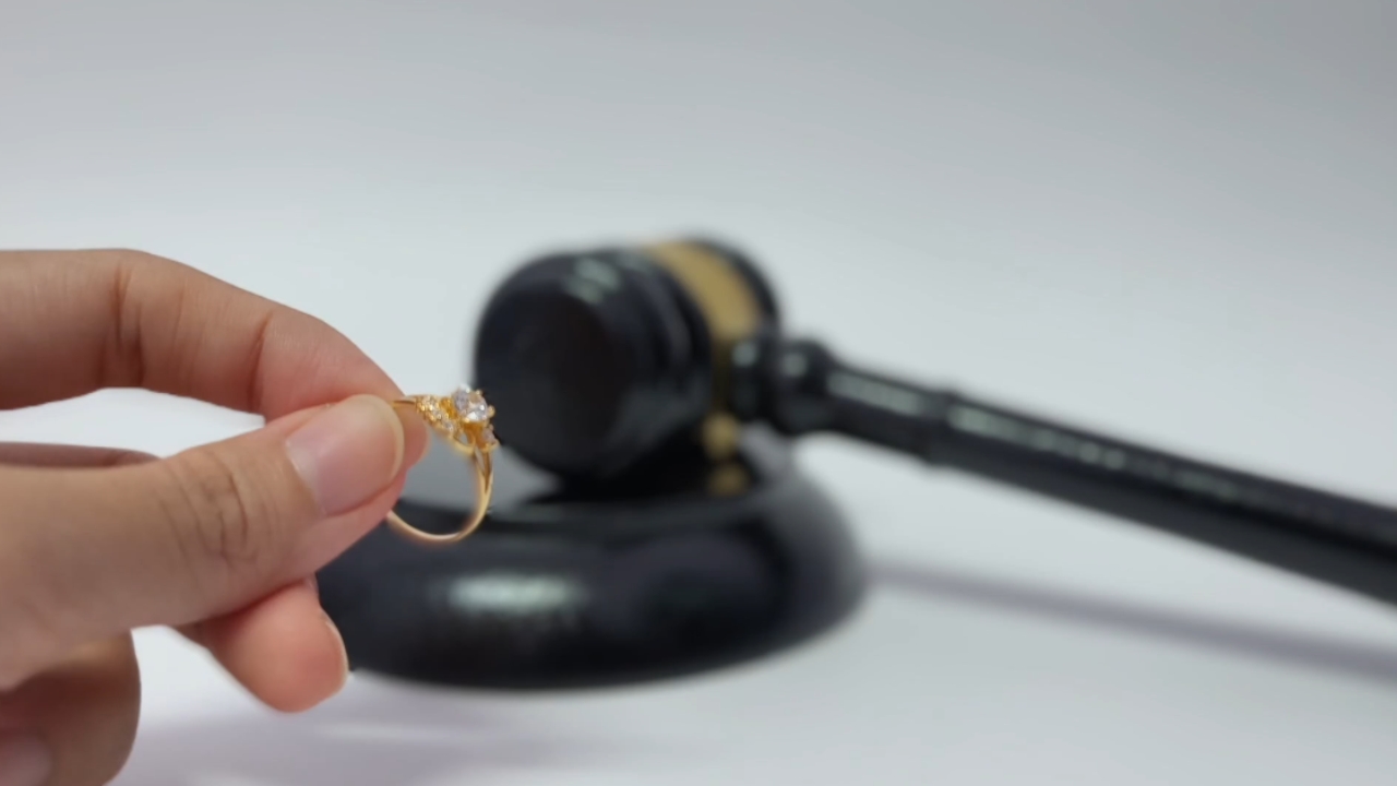 A hand holds a gold ring in front of a judge’s gavel