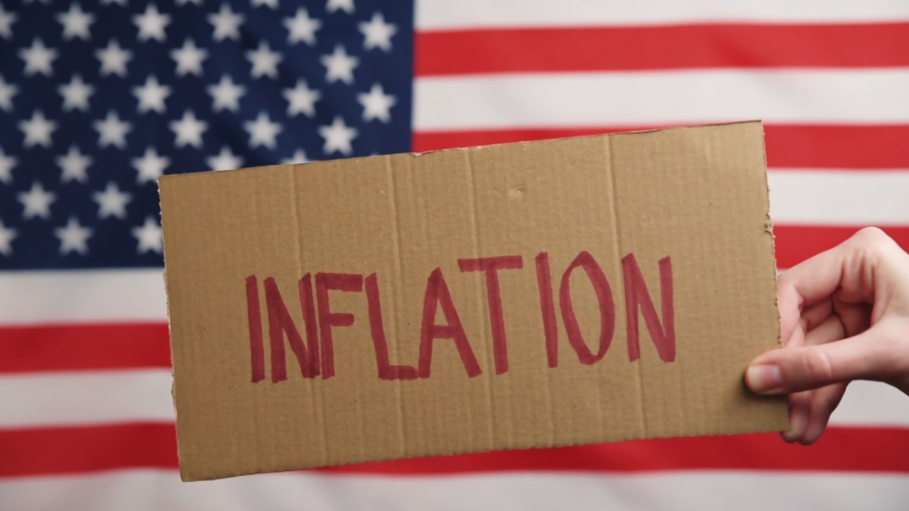 A hand holds an inflation sign in front of the American flag