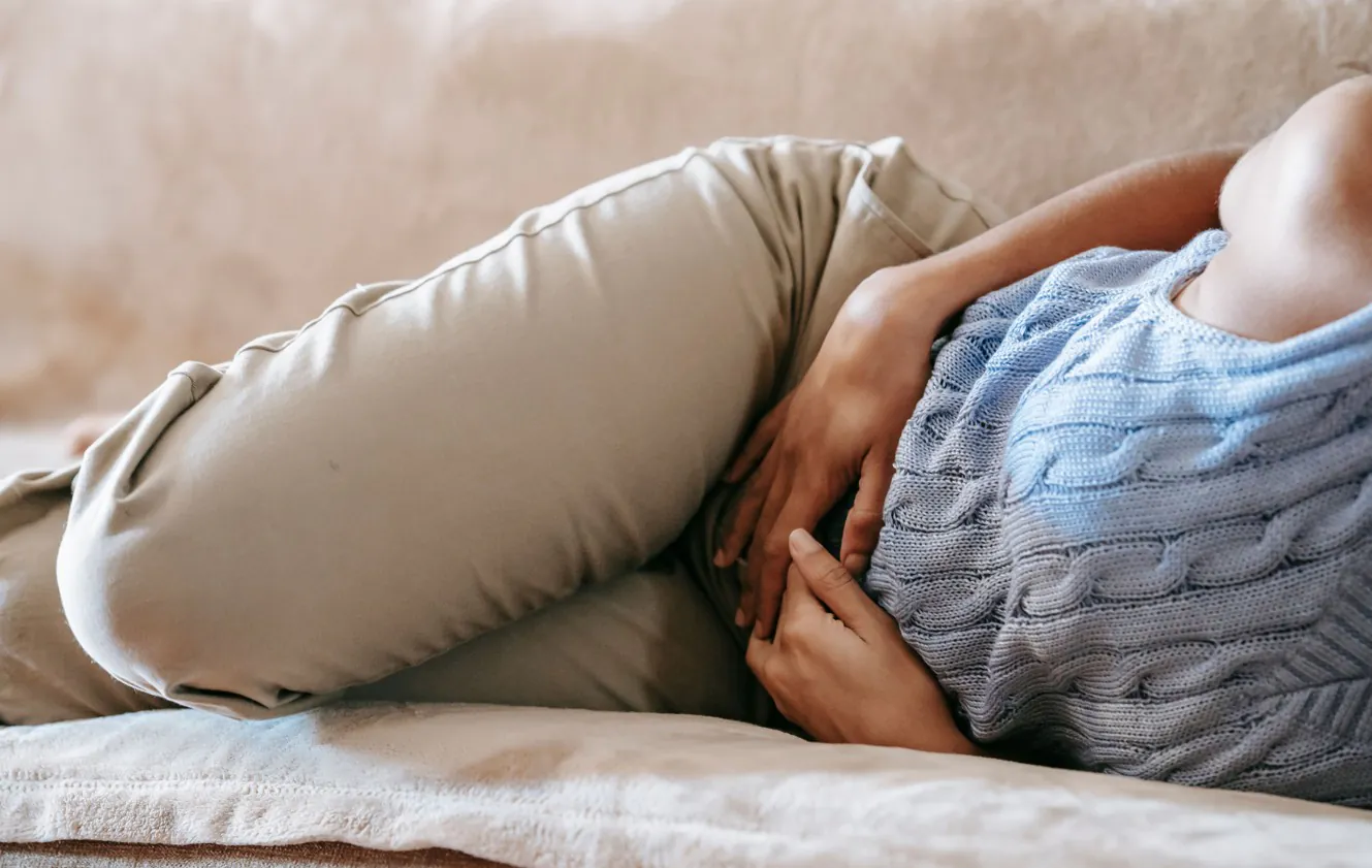 A woman with a stomach pain. Image used to visualise the symptoms of Cyclosporiasis