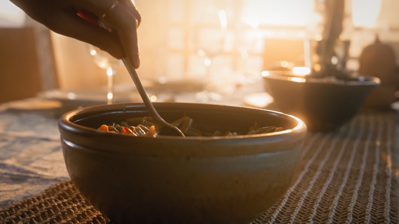 A person serves a bowl of soup at a sunlit dinner table