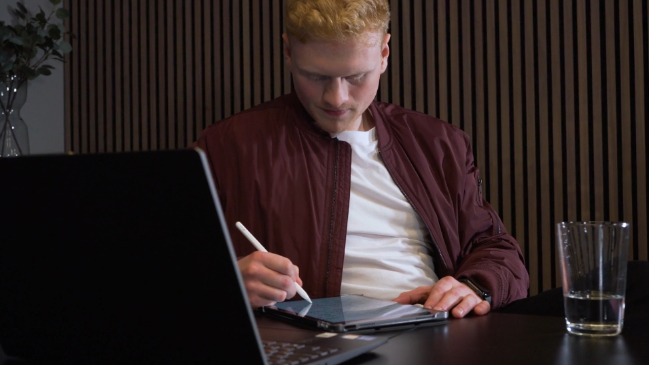 A college applicant uses a tablet beside a laptop at a desk