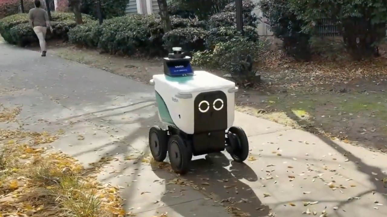 A delivery robot moves along a residential sidewalk