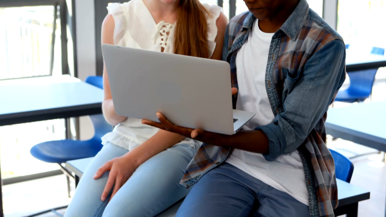 Two college students review a laptop in a campus study area