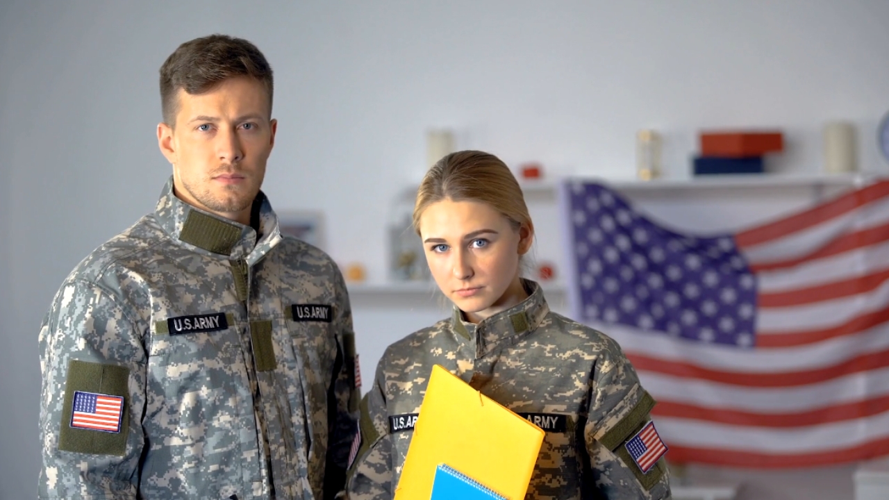 Two U.S. Army service members stand beside an American flag