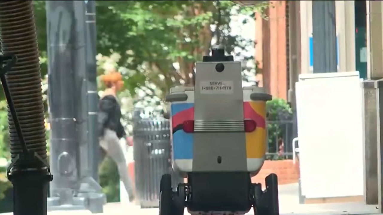 A delivery robot travels along a city sidewalk