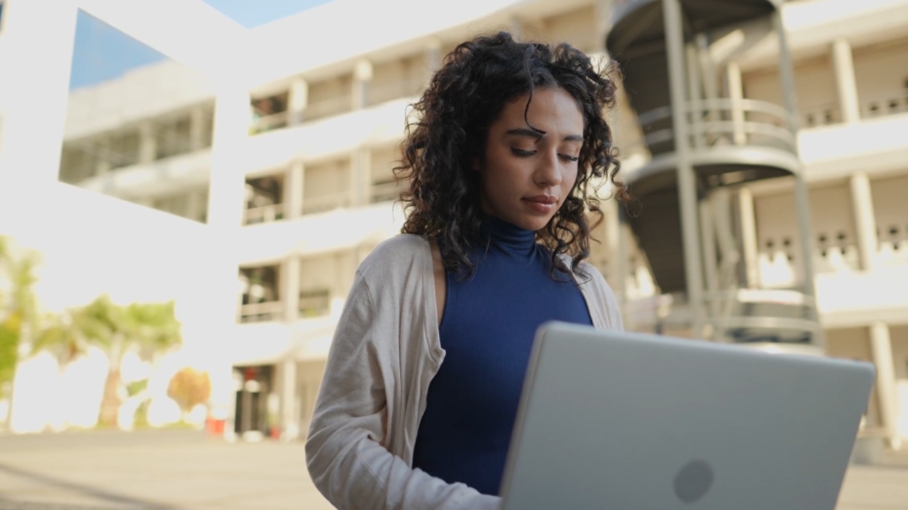 A college student checks a laptop outside a campus building