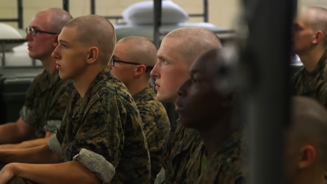 Marine Corps recruits sit in formation inside a classroom