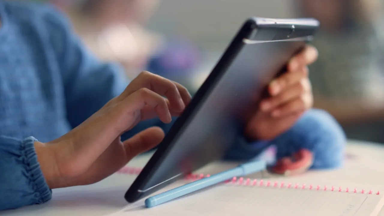 A student reviews college application materials on a tablet beside a notebook