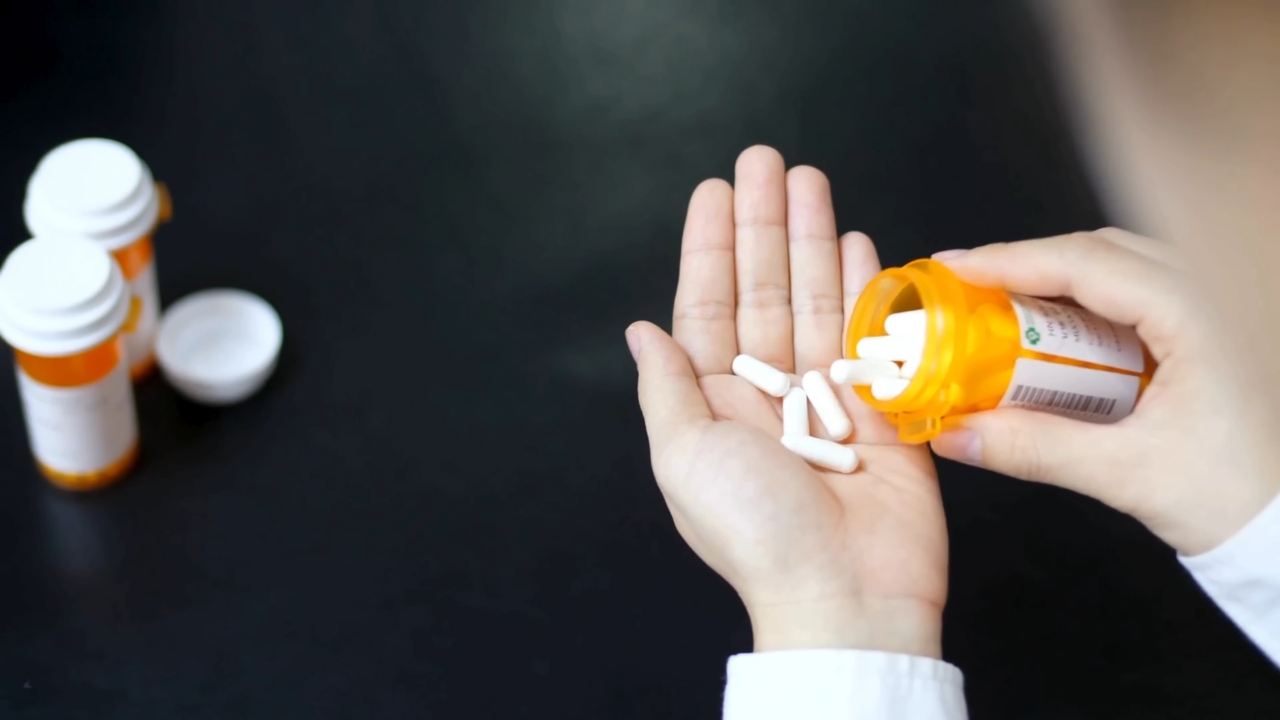 A person pours white capsules into their hand beside several medicine bottles
