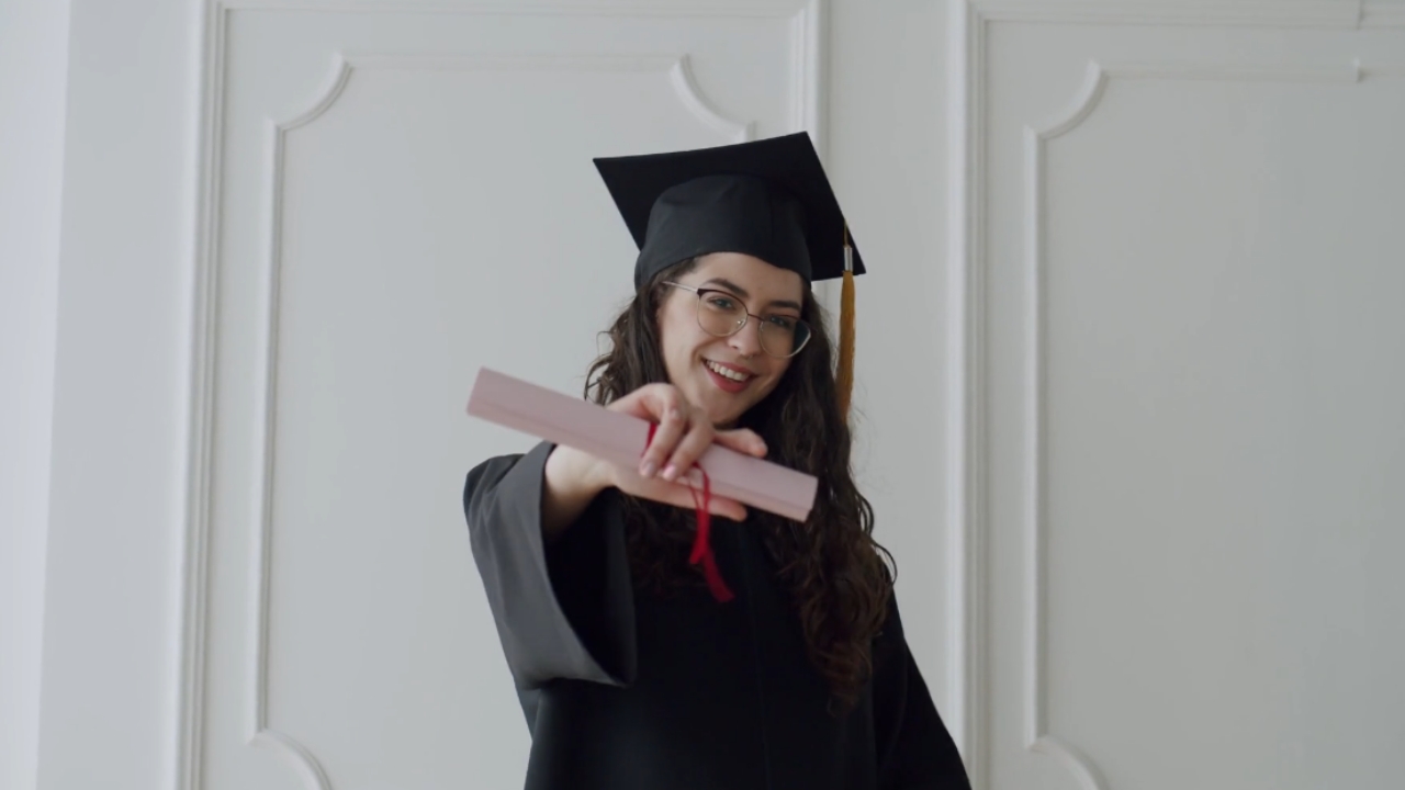 A graduate in a cap and gown holds out her diploma
