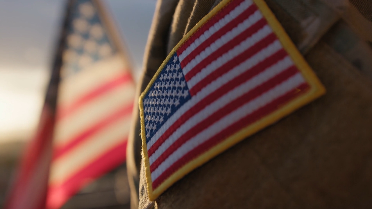 A U.S. flag patch appears on a military uniform beside an American flag