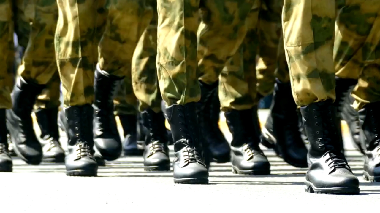 U.S. military personnel march in formation in camouflage uniforms and black boots