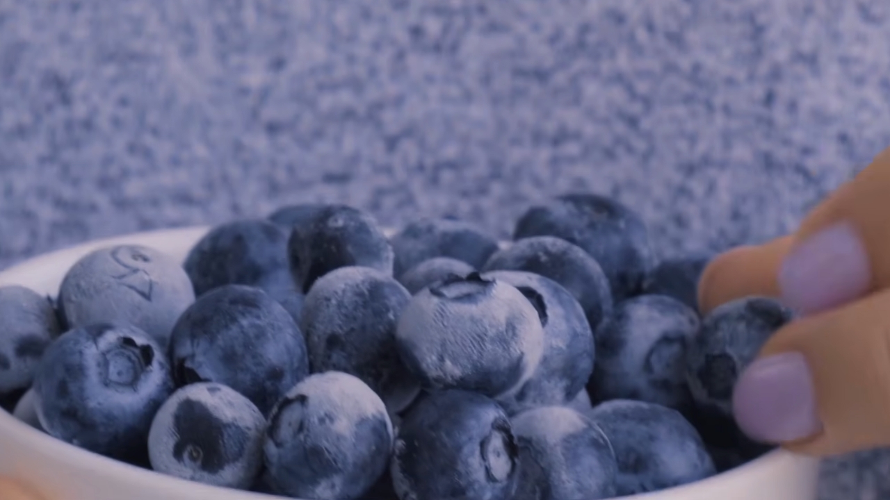 Frozen blueberries in a white bowl beside a hand