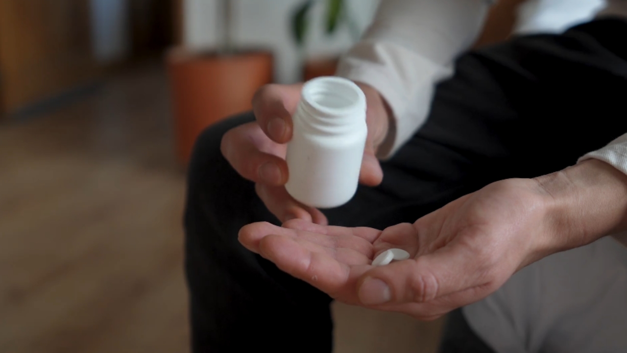 A person holds two white pills beside an open medication bottle