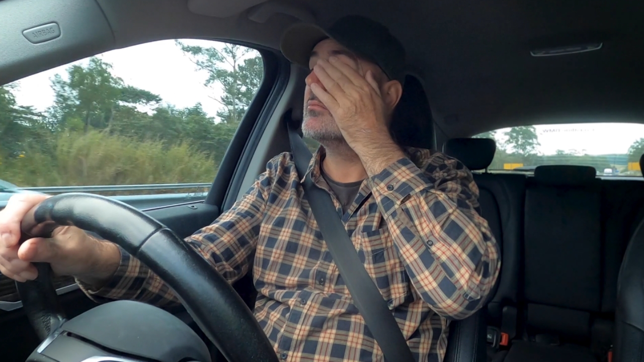 A tired driver covers his eyes behind the wheel on a highway