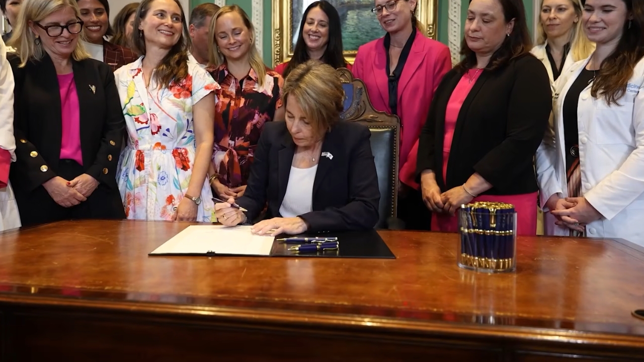 A governor signs an abortion bill at a desk as supporters stand nearby