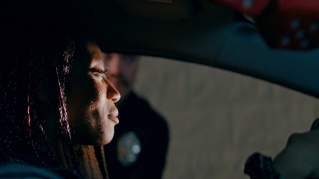 A driver sits behind the wheel at night as police lights reflect nearby