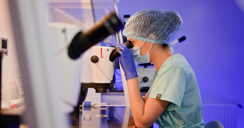 Researcher in protective clothing examining a laboratory sample through a microscope