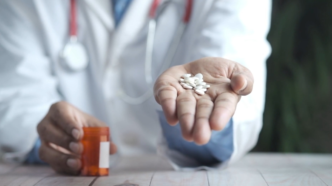 Doctor holds several white pills beside a prescription bottle