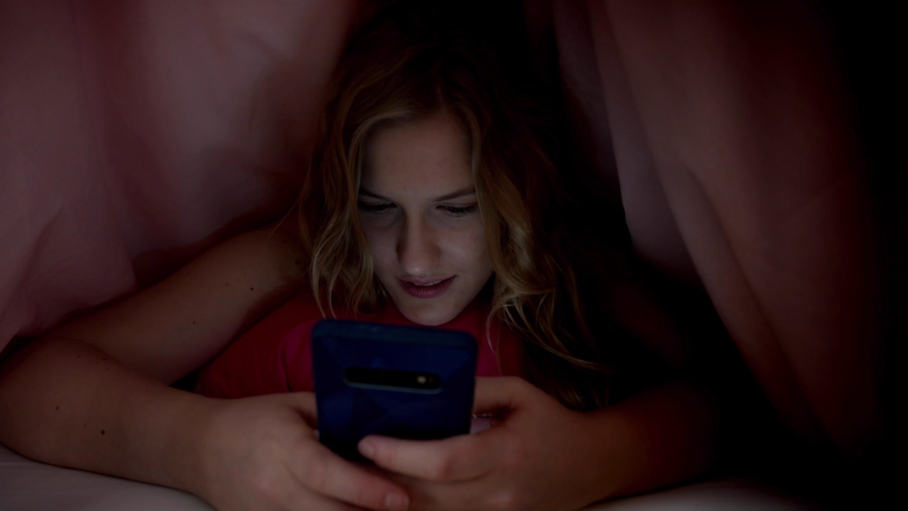 Young woman uses her smartphone in bed at night