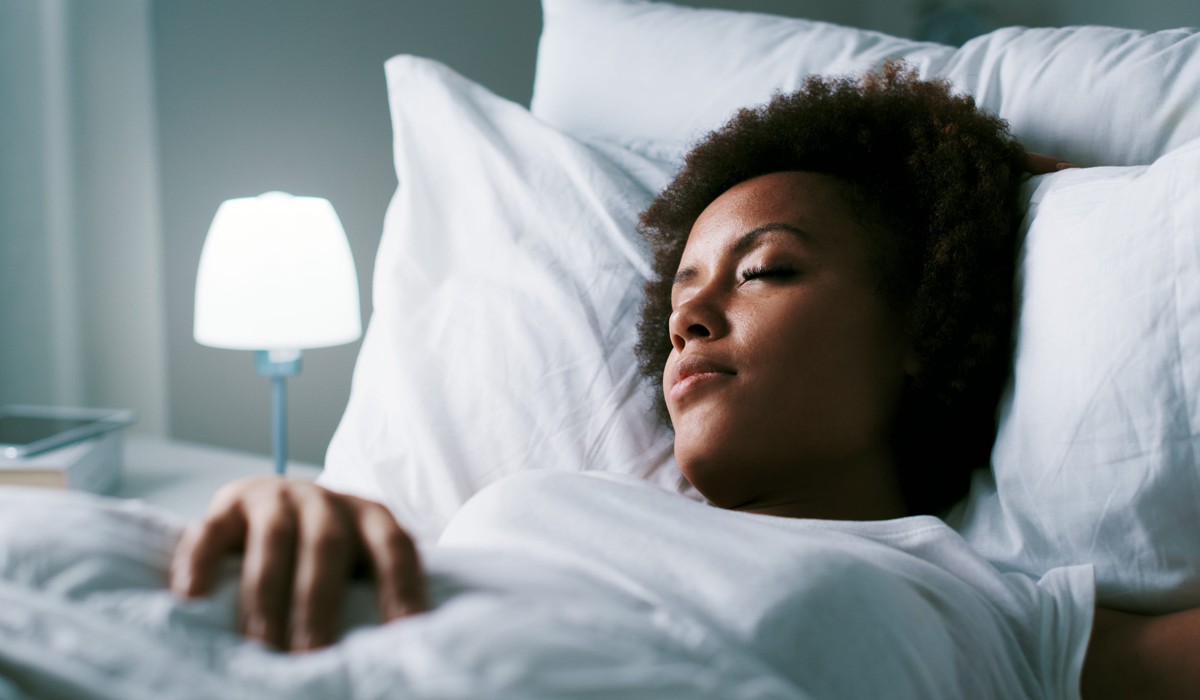 Young woman sleeping in her bed at night. An image used to visualize the latest research on whether there are side effects if you sleep with the lights on.