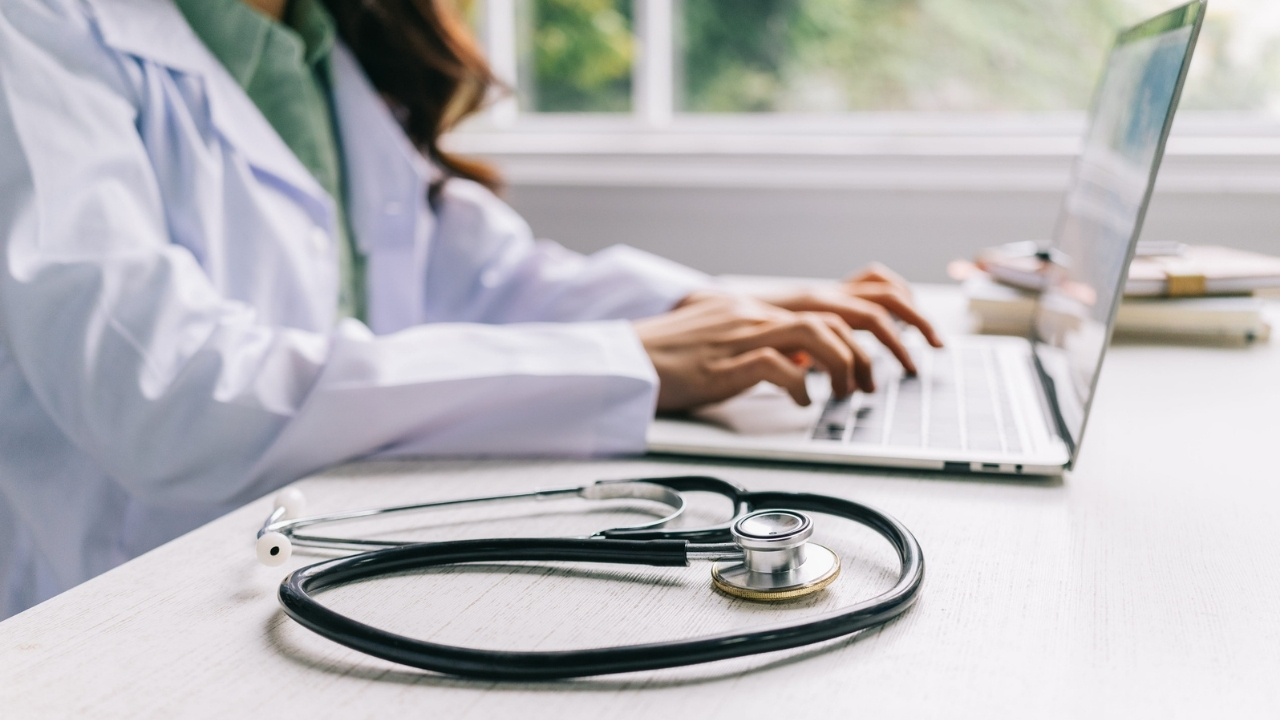 Doctor works on a laptop beside a stethoscope