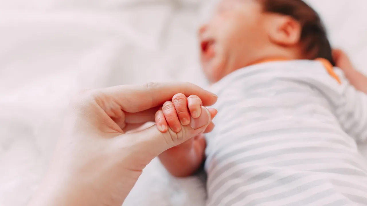 A newborn baby holds an adult’s finger.
