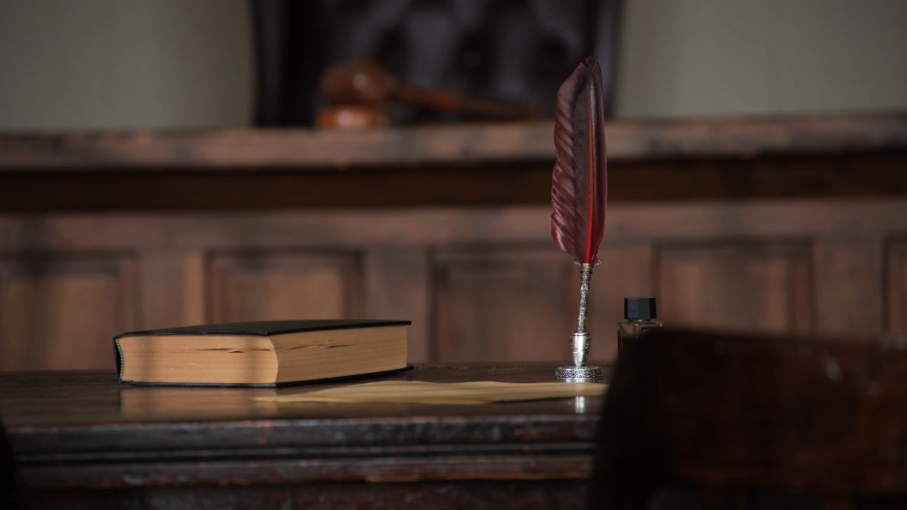 A law book and quill sit on a courtroom desk.