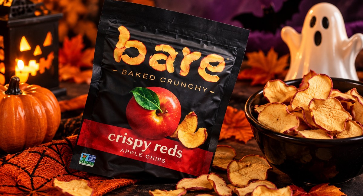 Bare Crispy Reds apple chips beside a black bowl of dried apple slices, with a Halloween ghost, pumpkin, autumn leaves and glowing lantern.