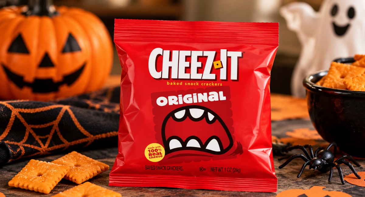 Red Cheez-It Original snack pack with cheese crackers, Halloween spiderweb decorations, a small ghost and a pumpkin in the background.